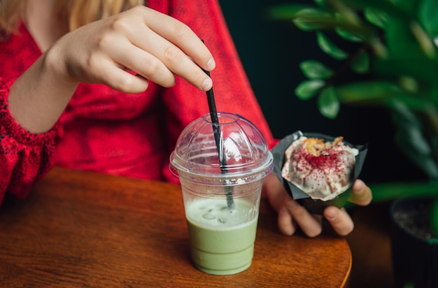 Primo piano di ghiaccio matcha latte e cupcake in un caffè in mani femminili