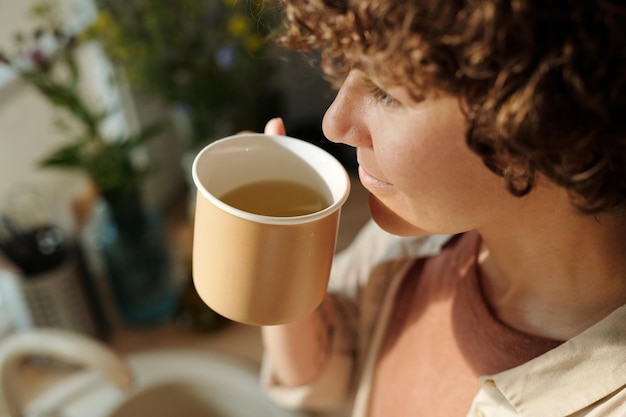 Primo piano di giovane donna bruna che mangia tisana calda al mattino soleggiato