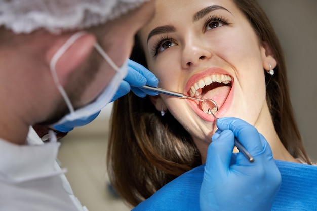 Primo piano di giovane donna con controllo dentale in studio dentistico. Dentista che esamina i denti di un paziente con strumenti dentali