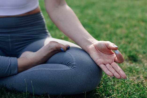 Primo piano di giovane donna seduta nella posizione del loto e meditando e con le dita in Gyan mudra all'alba al mattino nel parco.