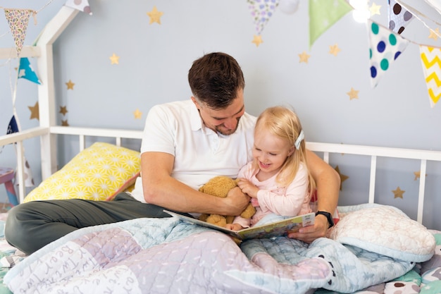 Primo piano di giovane papà del padre a letto con sua figlia felice del bambino che legge un libro