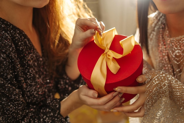 Primo piano di giovani mani femminili dalla pelle chiara di due ragazze in abiti che tengono una piccola confezione regalo Concetto di vacanza