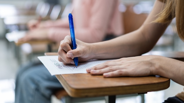 Primo piano di giovani studentesse universitarie si concentrano sul fare l'esame in classe. Una studentessa scrive la risposta degli esami sul foglio delle risposte in classe.
