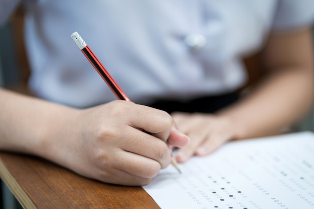 Primo piano di giovani studenti universitari si concentrano sul fare l'esame in classe. La studentessa scrive sulla carta di risposta agli esami in classe.