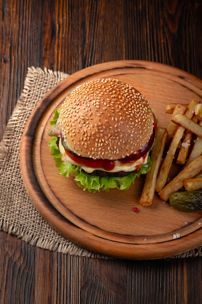 Primo piano di hamburger fatto in casa con carne di manzo, pomodoro, lattuga, formaggio e patatine fritte sul tagliere