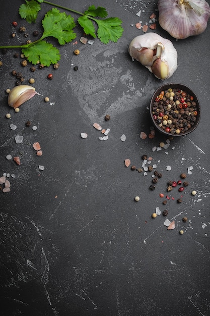 Primo piano di ingredienti da cucina tradizionali: aglio, olio d'oliva, sale, pepe, erbe fresche su fondo rustico scuro. Cornice per alimenti, concetto per cucinare cibi sani con spazio per il testo, vista dall'alto