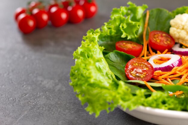 Primo piano di insalata di foglie verdi con carote pomodoro cipolla cavolfiore con pomodori in background