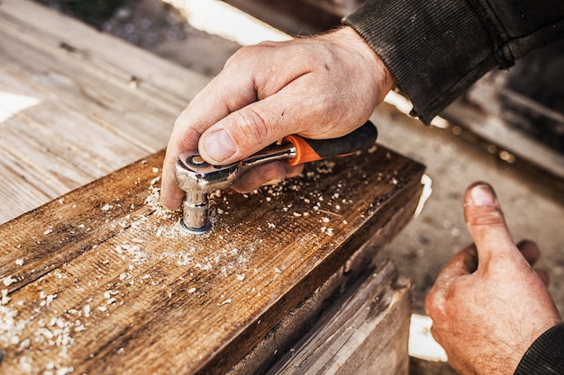 Primo piano di mani avvitando un bullone in una tavola di legno