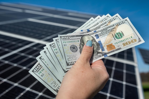 Primo piano di mani che tengono denaro su pannelli solari sullo sfondo Il concetto di risparmio energetico e consumo sostenibili