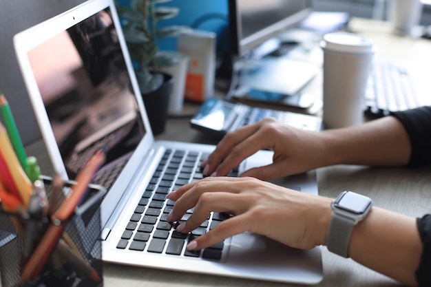 Primo piano di mani femminili impegnate a digitare sul computer portatile in un ufficio moderno.