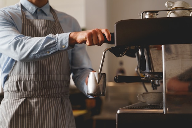 Primo piano di mani maschili che tengono una tazza metallica argentata e versano bevande calde dal rubinetto della macchina da caffè