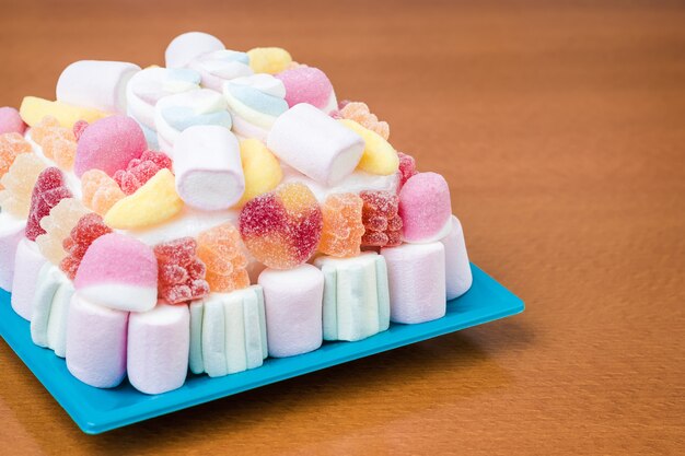 Primo piano di marshmallow e torta di fagioli di gelatina su un piatto blu per una festa per bambini, in tenui toni pastello
