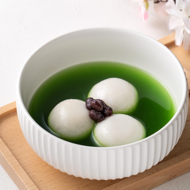 Primo piano di matcha big tangyuan (tang yuan) con zuppa di matcha dolce e pasta di fagioli rossi in una ciotola su sfondo bianco da tavola per cibo da festival.