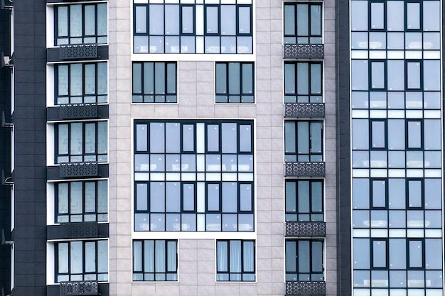 Primo piano di molte finestre su una facciata grigia di un moderno condominio. Per sfondo immobiliare.