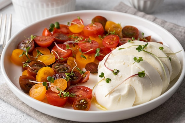 Primo piano di mozzarella con pomodorini a fette, condito con olio d'oliva, piatto bianco con insalata caprese.