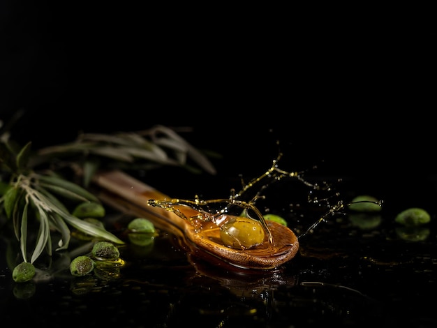 Primo piano di oliva verde con spruzzi di olio su un cucchiaio di legno su uno sfondo scuro