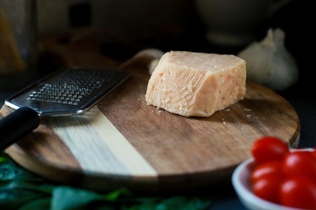 primo piano di parmigiano su tavola di legno con pomodori, basilico, pasta e grattugia