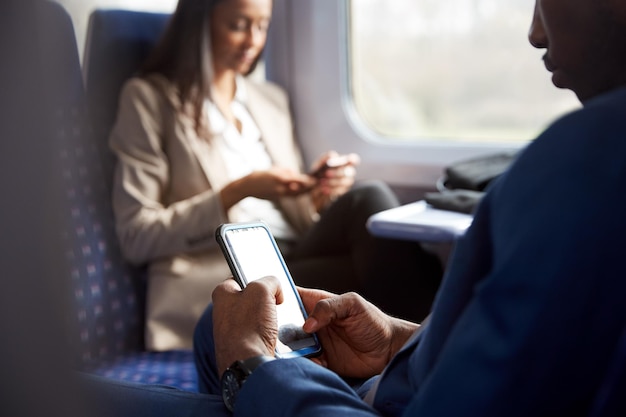 Primo piano di passeggeri d'affari seduti in treno che si recano al lavoro guardando i telefoni cellulari