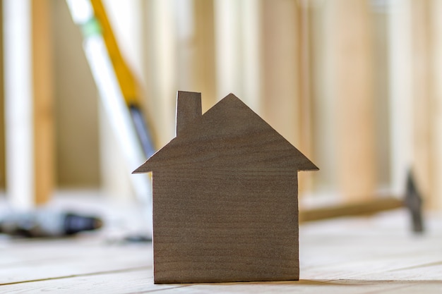 Primo piano di piccola casa di modello marrone semplice sul fondo vago degli strumenti della costruzione. Costruzione, costruzione e investimenti immobiliari, proprietà e proprietà del concetto di casa dei sogni.