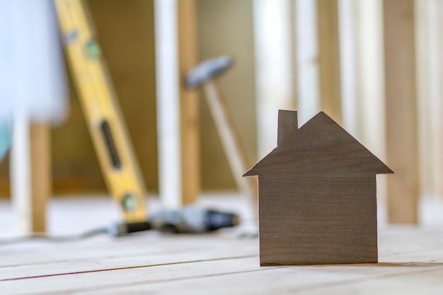 Primo piano di piccola casa di modello marrone semplice sul fondo vago degli strumenti della costruzione. Costruzione, costruzione e investimenti immobiliari, proprietà e proprietà del concetto di casa dei sogni.