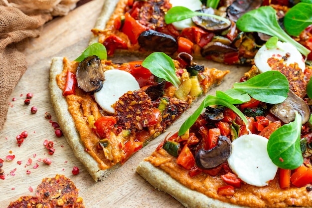 Primo piano di pizza fresca vegana cruda con funghi e altre verdure servite su una tavola di legno