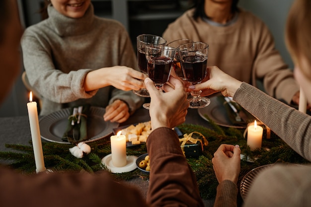 Primo piano di quattro amici che si godono la cena di Natale insieme e brindano con bicchieri di vino seduti...