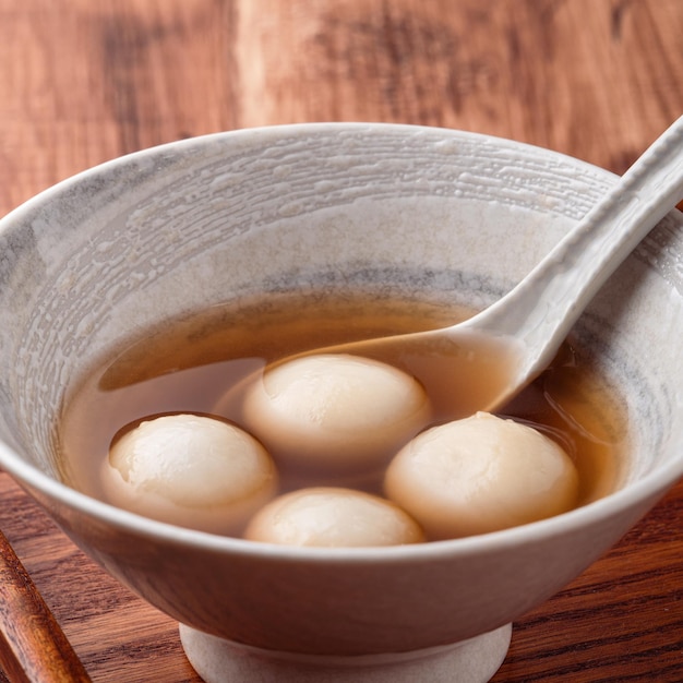 Primo piano di sesamo grande tangyuan (tang yuan, palline di gnocco di riso glutinoso) con zuppa di sciroppo dolce in una ciotola sul fondo della tavola di legno per il cibo del festival del solstizio d'inverno.