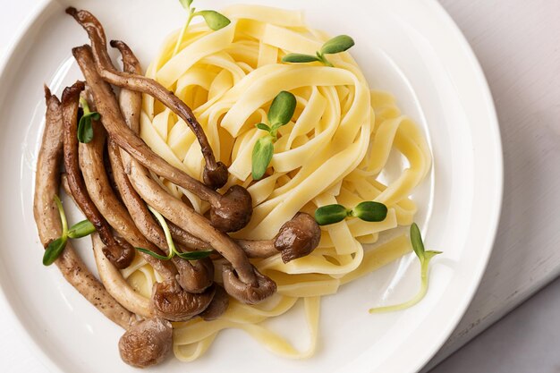 Primo piano di shimeji cotto e piatto di tagliatelle con funghi e pasta fritti