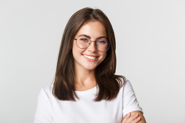 Primo piano di sorridente fiduciosa, bella ragazza bruna con gli occhiali che sembra felice.