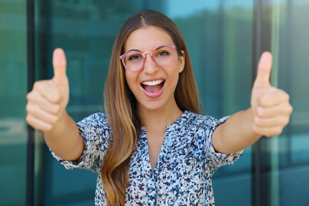 Primo piano di successo vincente giovane donna con i pollici in su all'aperto