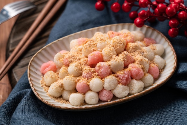 Primo piano di tangyuan rosso e bianco fritto (tang yuan, palline di gnocchi di riso glutinoso) con polvere di arachidi su sfondo di tavolo in legno per il cibo del festival del solstizio d'inverno.