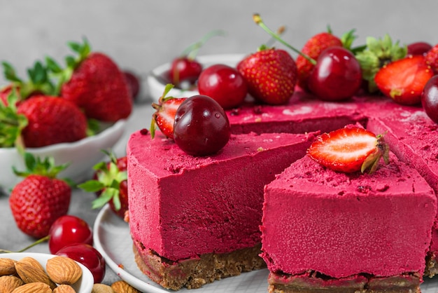 Primo piano di torta di anacardi a base di bacche vegane crude affettate con fragole fresche e ciliegie Cibo vegetariano sano