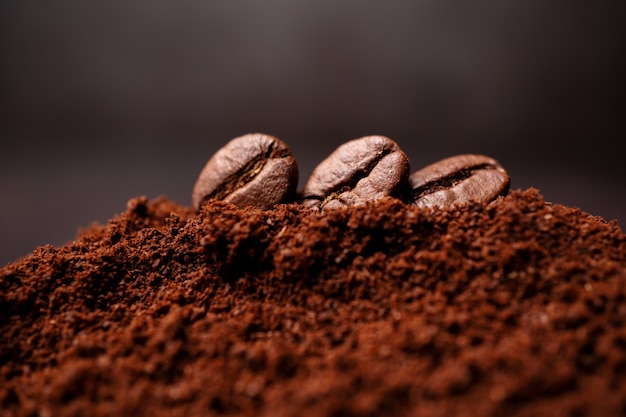 Primo piano di tre chicchi di caffè al mucchio misto di caffè tostato