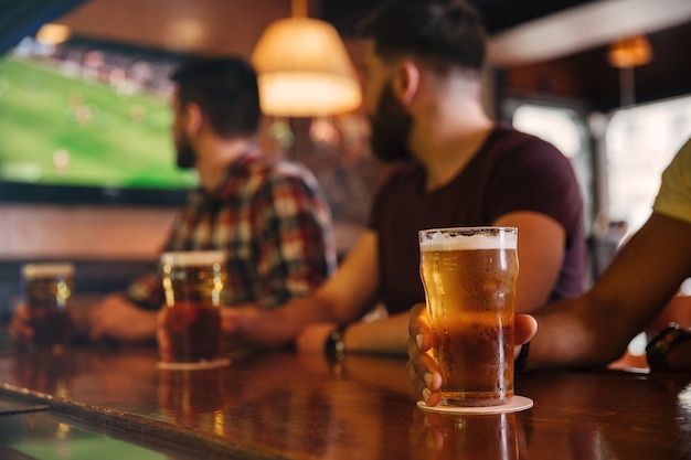 Primo piano di tre giovani uomini che bevono birra al bar e guardano la partita di calcio