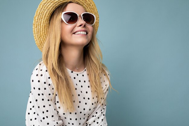 Primo piano di un'affascinante giovane donna bionda positiva sorridente che indossa un cappello di paglia vestito estivo e