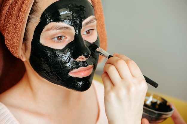 Primo piano di un'applicazione della maschera cosmetica sul viso della donna indossa un asciugamano sulla testa.