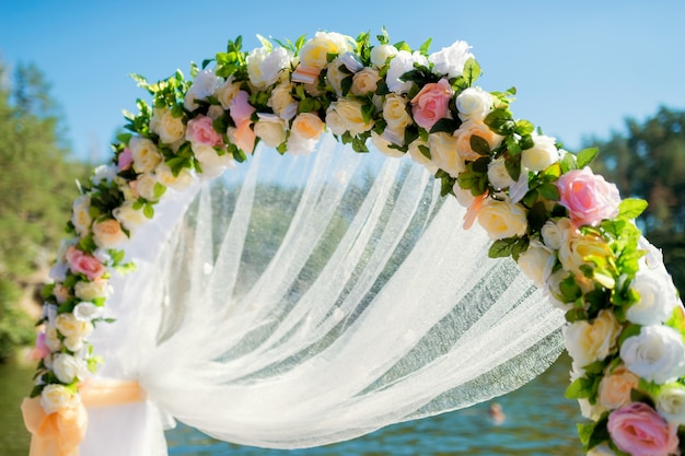 Primo piano di un arco di nozze decorato con fiori teneri e panno bianco fuori sotto il cielo blu.