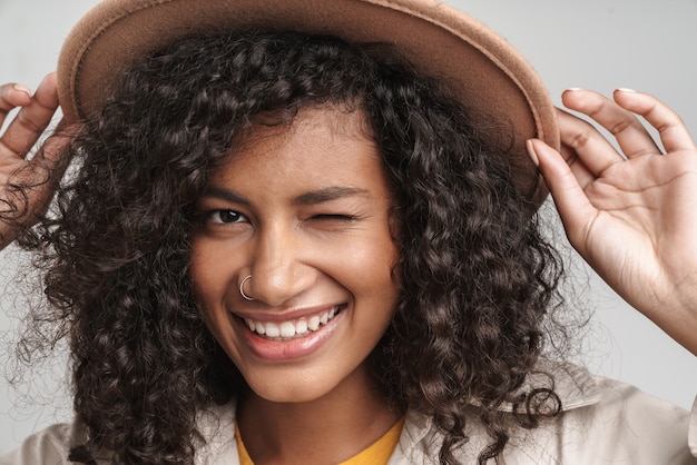 Primo piano di un'attraente giovane donna africana sorridente con i capelli ricci, che indossa un cappotto autunnale e un cappello