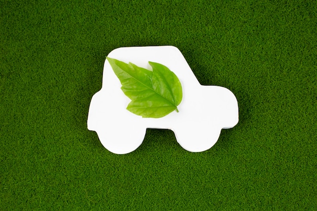 Primo piano di un'auto bianca con foglia verde su sfondo erboso Concetto di trasporto automobilistico ecologico salva l'ambiente Salva la terra