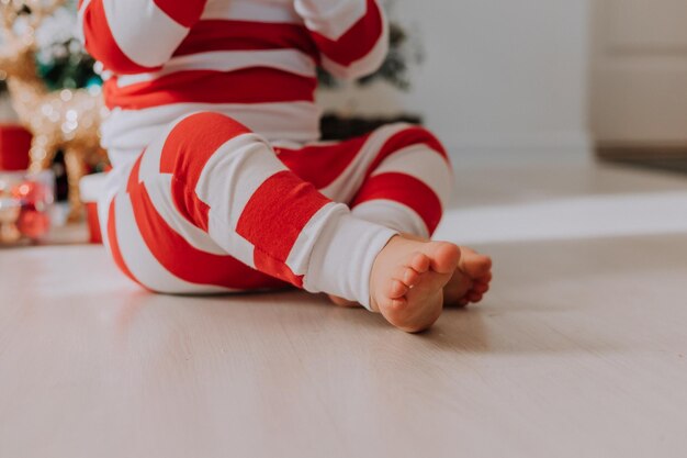 Primo piano di un bambino a piedi nudi in pigiama a righe di Natale seduto su un pavimento di legno