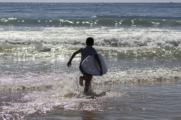 Primo piano di un bambino che corre verso il mare con una tavola da surf