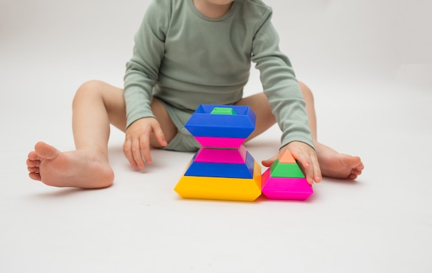 Primo piano di un bambino piccolo che gioca con una piramide colorata su sfondo bianco
