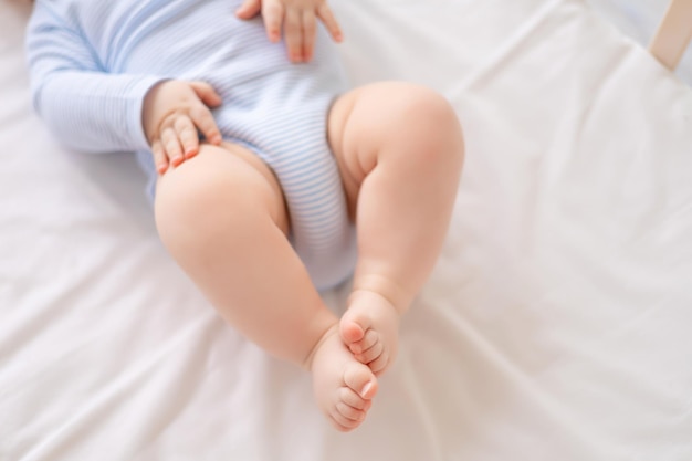 Primo piano di un bambino piccolo che si trova in una culla sulle gambe bianche della biancheria da letto di un bambino sano