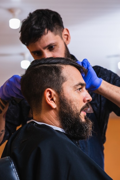 Primo piano di un barbiere che taglia i capelli di un uomo nel negozio di barbiere - Profilo di un giovane uomo con la barba in un negozio di barbiere.