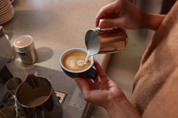 Primo piano di un barista irriconoscibile che crea arte del latte con crema mentre prepara caffè fresco in un bar o in una caffetteria, copia spazio