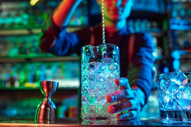 Primo piano di un barman professionista che finisce la preparazione di cocktail alcolici in luce al neon multicolore, lo dà al cliente. Intrattenimento, bevande, concetto di servizio. Bar moderno, colori neon alla moda.