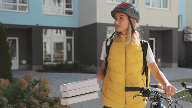 Primo piano di un bell'uomo che apre la porta a una donna di consegna della pizza che indossa uno zaino termico giallo su una bicicletta e riceve scatole di cartone di pizza Concetto di consegna del cibo
