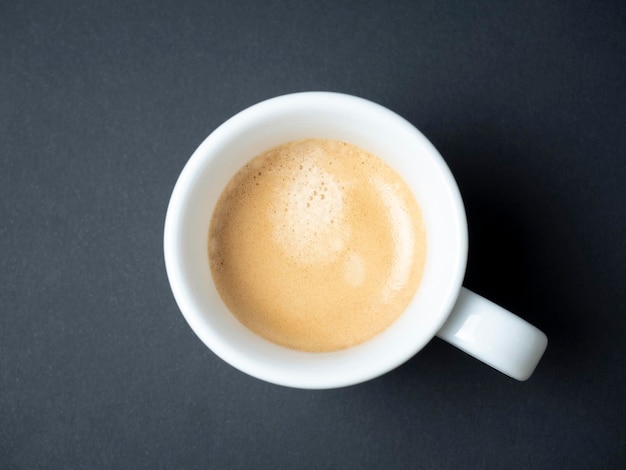 Primo piano di un caffè profumato in una tazza bianca su sfondo nero Schiuma marrone vista dall'alto piatto