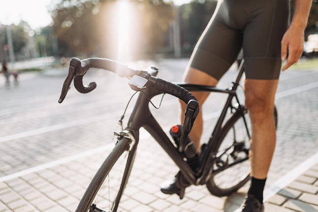 Primo piano di un ciclista professionista in abiti sportivi che riposa sulla sua bici dopo l'allenamento all'aperto Luce solare estiva sullo sfondo Concetto di stili di vita attivi