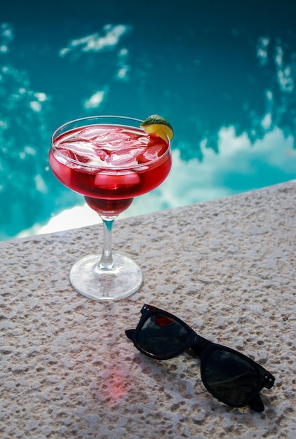 primo piano di un cocktail rosso rinfrescante con occhiali da sole neri in piscina